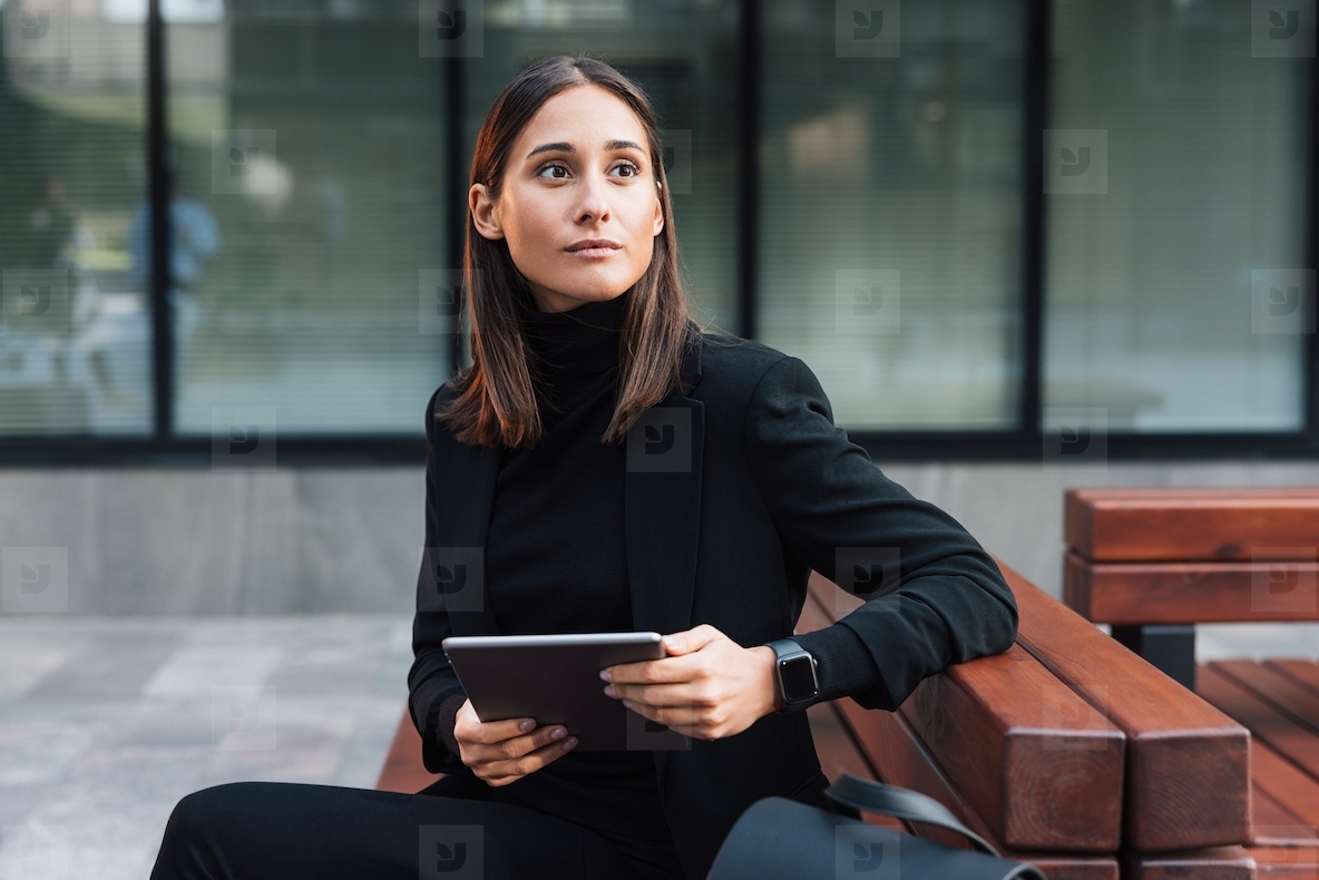 Serious and stylish woman sitting outdoors with a digital tablet and looking away