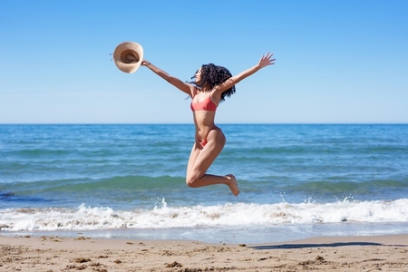 Joyful Summer Moments A Woman Joyfully Leaping on the Beach Wearing a Straw Hat Joyful Summer Moments A Woman Joyfully Leaping on the Beach Wearing a Straw Hat