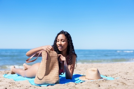 A Young Woman is Enjoying a Relaxing Day on the Beach with a Tote Bag under a Clear Blue Sky