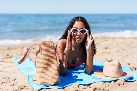 A Young Woman is Relaxing on the Beach  Wearing Stylish Sunglasses and Carrying a Beach Bag