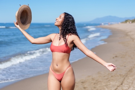 A joyful woman enjoys the beach soaking up the sun in her bright colorful summer attire A joyful woman enjoys the beach soaking up the sun in her bright colorful summer attire