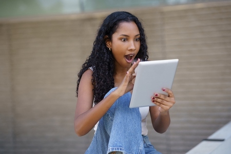 A Surprised Young Woman Engaged with a Tablet While Enjoying an Outdoor Setting Surrounded by Nature