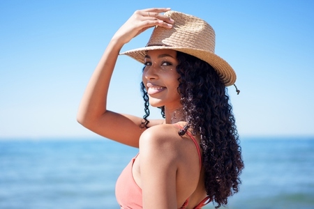 A Joyful Woman Wearing a Beautiful Straw Hat at the Beach  Enjoying the Warm Sunshine