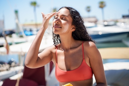 A young woman is seen applying sunscreen by the water during a beautiful sunny day
