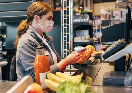 Female cashier in mask using barcode scanner at checkout