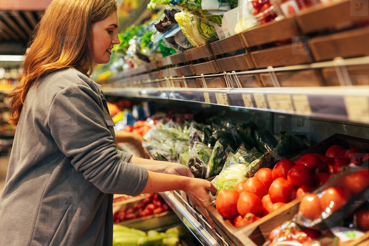 Female grocery store worker refreshing products on the shelf moving a box