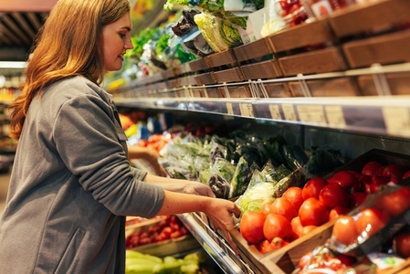 Female grocery store worker refreshing products on the shelf  moving a box