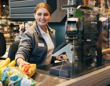 Smiling female cashier working at the cash register and moving scanned products
