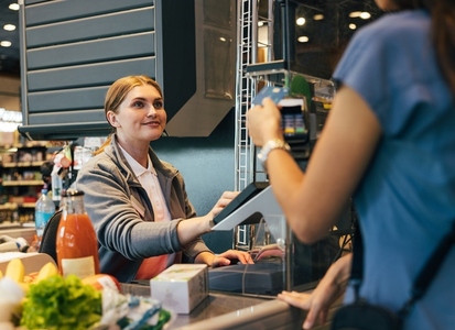 Smiling female cashier accepting payment from customer entering data into terminal Smiling female cashier accepting payment from customer entering data into terminal