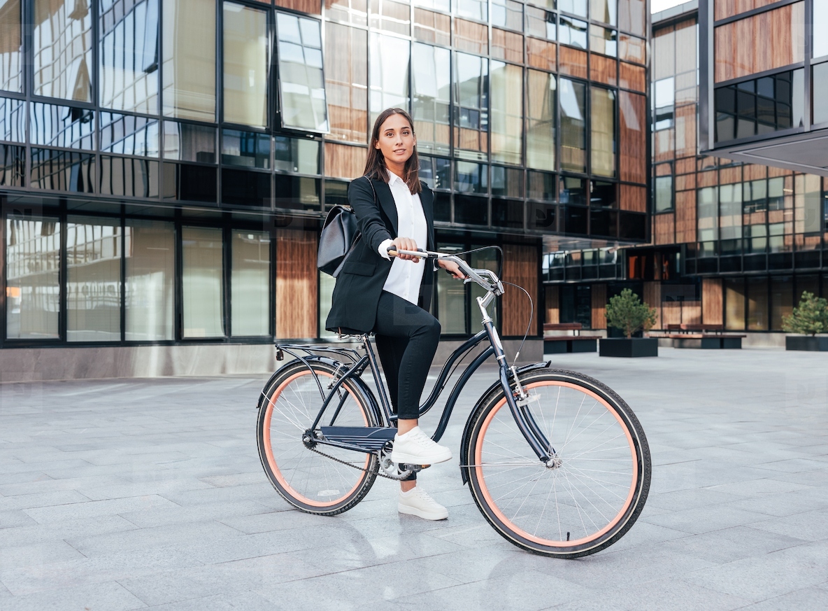 Stylish businesswoman with a bicycle standing in the city wearing a backpack and black office attire