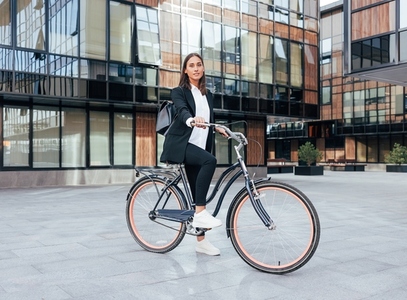 Stylish businesswoman with a bicycle standing in the city wearing a backpack and black office attire