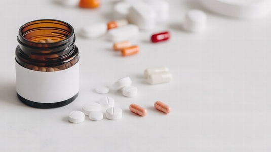 Brown pill bottle with white label and various pills scattered on white surface