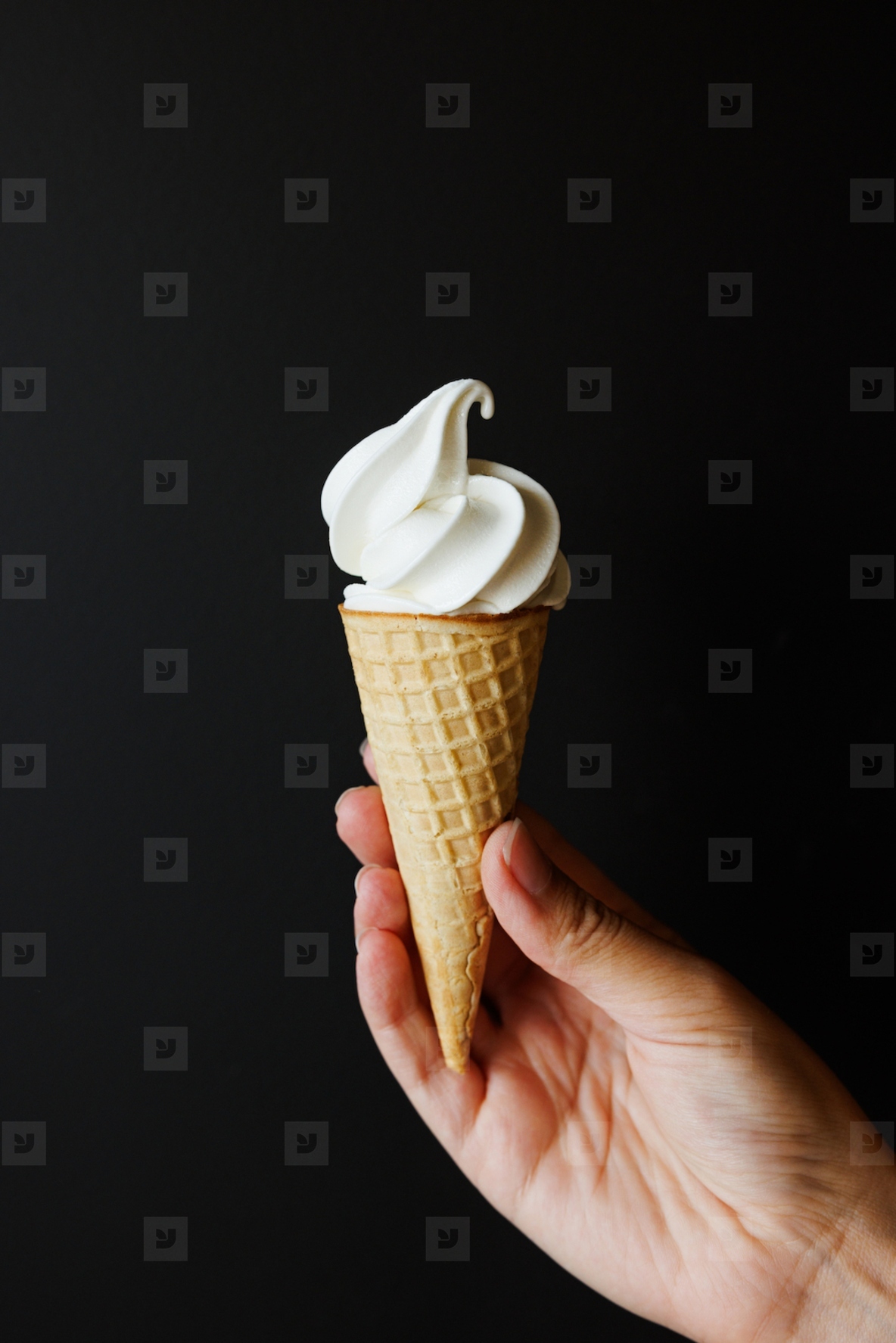 Hand of an unrecognizable person holding an ice cream cone over a black background