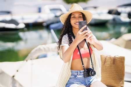 A Young Woman Capturing a Candid Selfie by the Marina While Dressed in a Summer Outfit