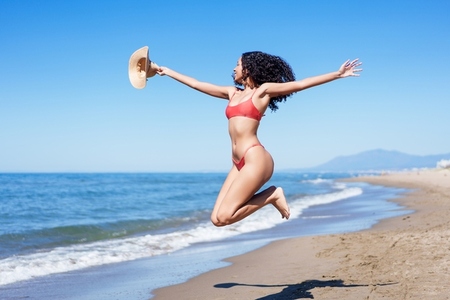 A Joyful Woman Happily Jumping on the Beach During a Bright and Warm Summer Day in Paradise A Joyful Woman Happily Jumping on the Beach During a Bright and Warm Summer Day in Paradise
