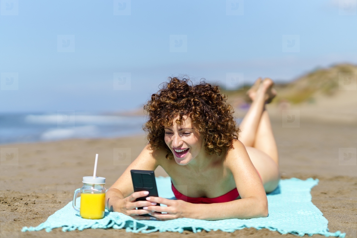 Laughing woman using smartphone while lying on beach