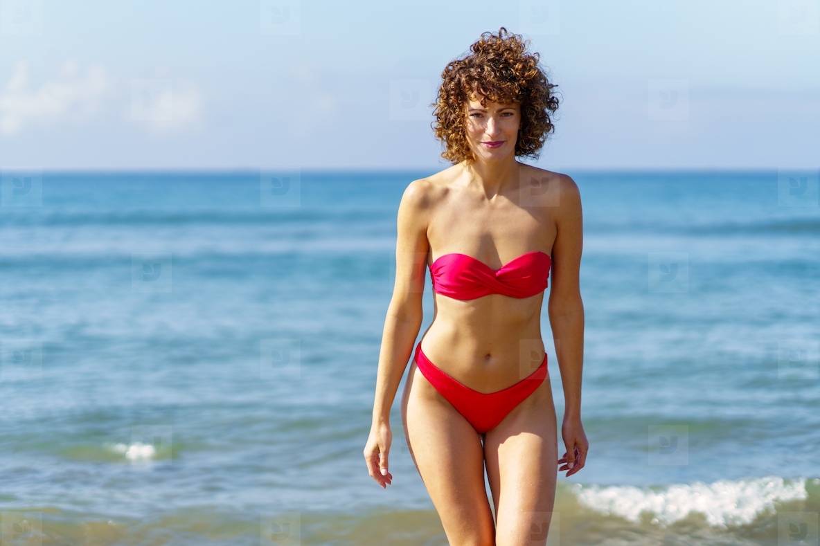 Slim woman in red bikini standing near sea