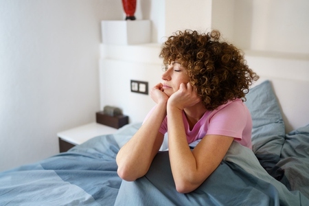 Curly female with closed eyes sitting on bed Curly female with closed eyes sitting on bed