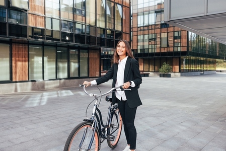 Young smiling woman in business attire with a bicycle standing in the city