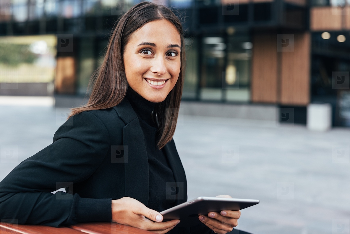 Smiling brunette woman in black formal clothes sitting outdoors with digital tablet