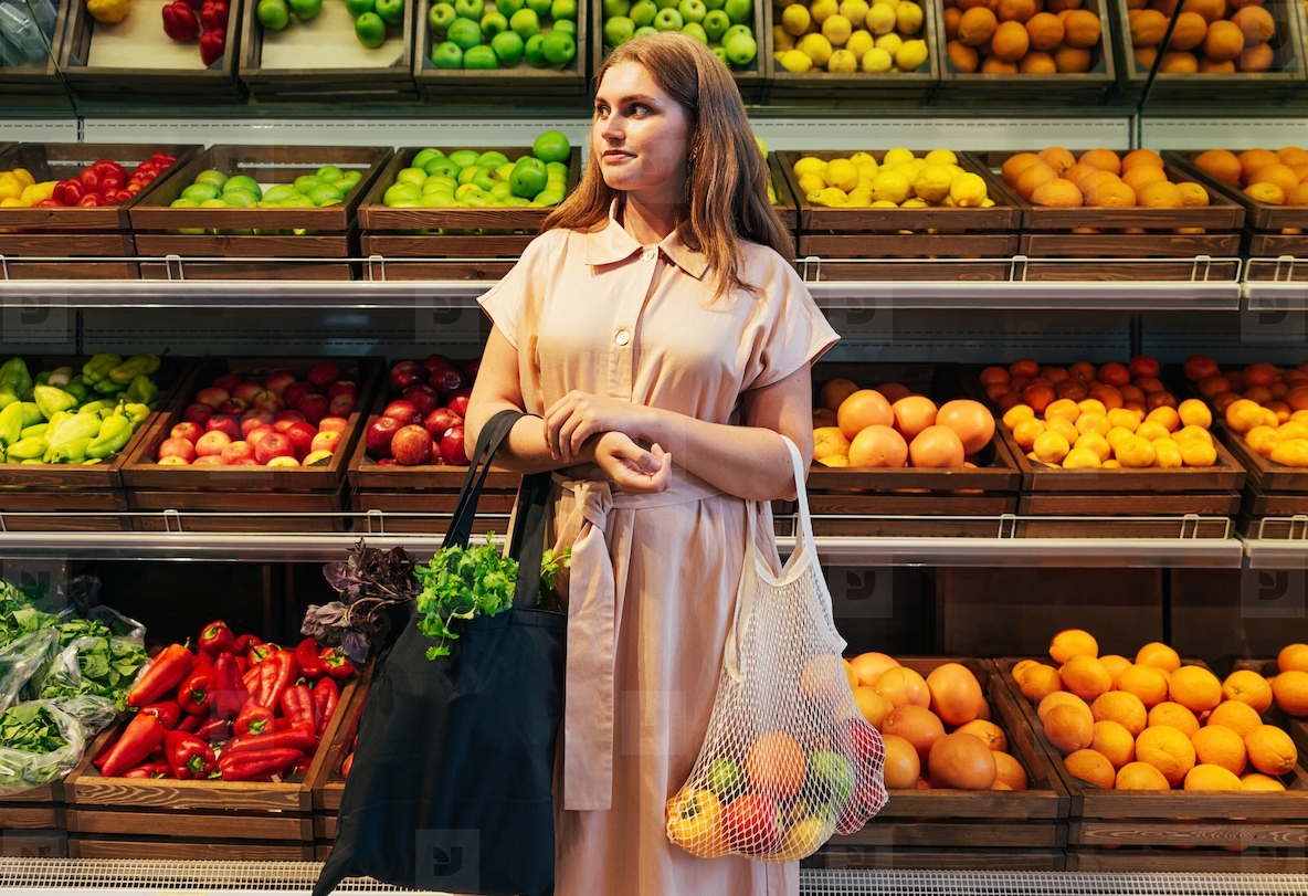 Female customer with bags full of vegetables and fruits standing in front of the shelves in the grocery store