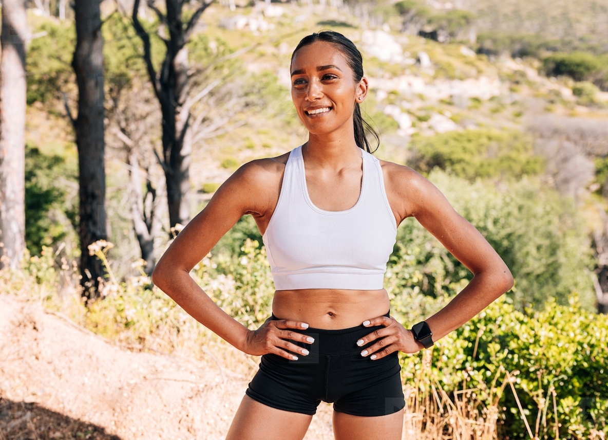 Young smiling female with hands on her hips standing confidently ina natural park during workout