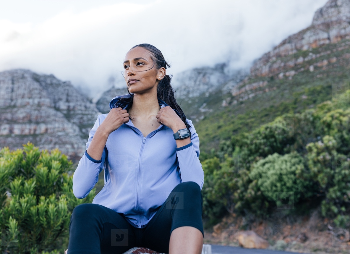 Young sportswoman adjusting her fitness attire while relaxing during a workout in natural park