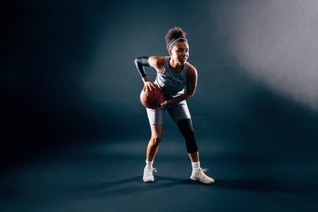 Professional female basketball player in uniform with ball over dark background in studio