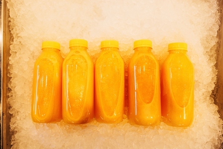 Five bottles with orange juice on the ice  shot from above