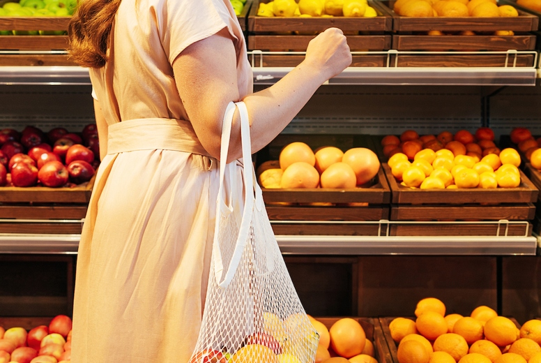 Back view of young woman choosing fruits while standing at shelves in grocery store