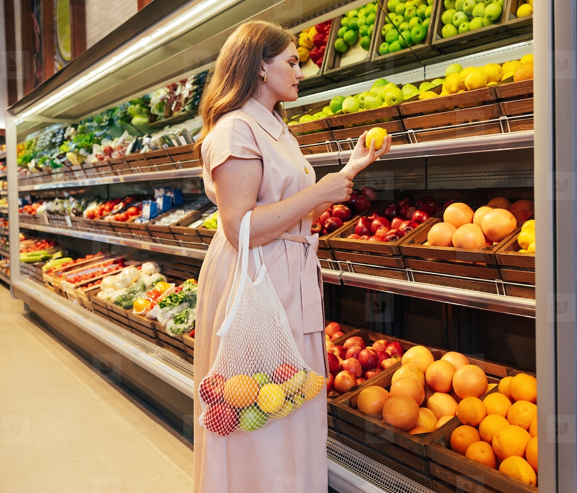 Young woman with string bag in grocery store  Female holding a lemon while standing at shelves in a grocery store