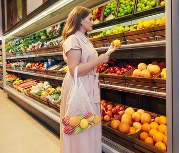 Young woman with string bag in grocery store  Female holding a lemon while standing at shelves in a grocery store