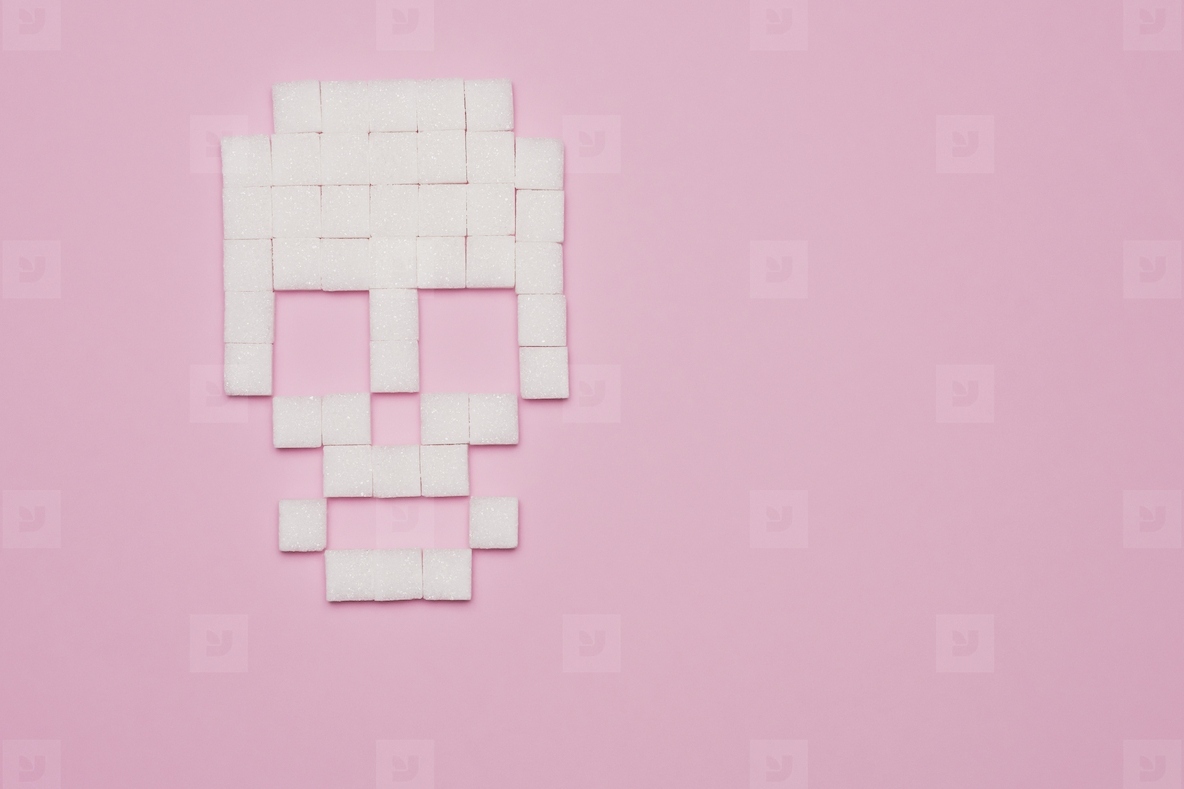 Still life concept of white sugar cubes forming skull on pink background with copy space