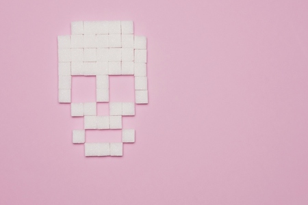 Still life concept of white sugar cubes forming skull on pink background with copy space