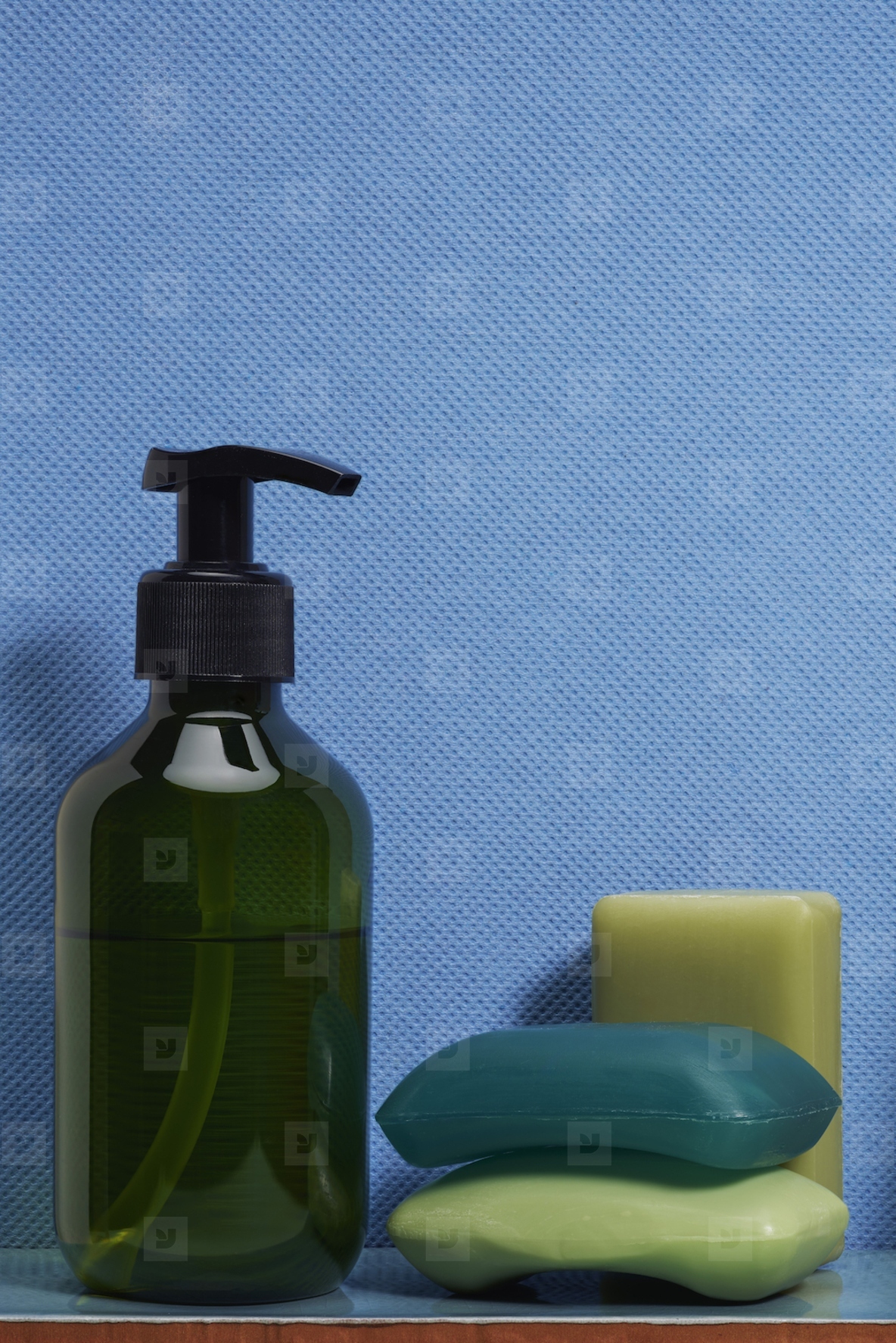 Still life of green liquid hand soap and homemade soap bars against textured blue background