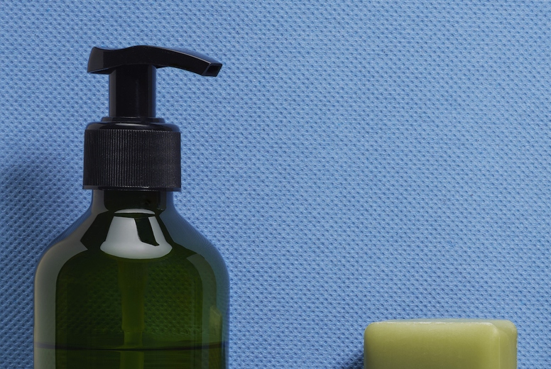 Still life of green liquid hand soap and homemade soap bars against textured blue background