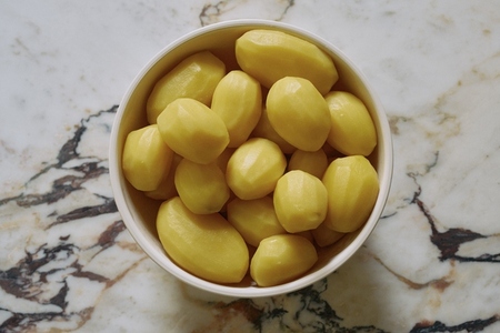 Still life view from above of raw golden peeled potatoes in bowl on granite surface