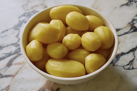 Still life shot of small raw peeled potatoes in bowl on granite counter