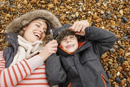 Happy mother and son in fur lined hoods laying on rocky beach Happy mother and son in fur lined hoods laying on rocky beach