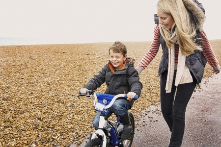 Happy mother helping son learn how to ride bicycle on path along rocky beach Happy mother helping son learn how to ride bicycle on path along rocky beach