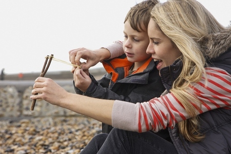 Mother teaching son how to use slingshot on rocky beach