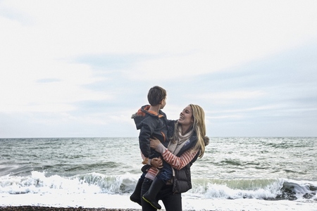 Happy carefree mother holding son on winter beach