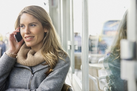 Smiling blond woman talking on smart phone at sidewalk cafe