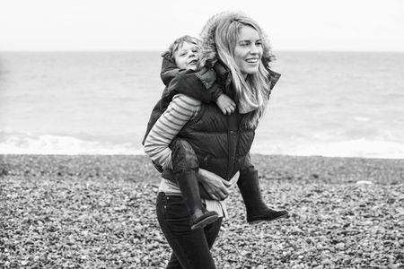 Happy mother piggybacking cute son on rocky beach
