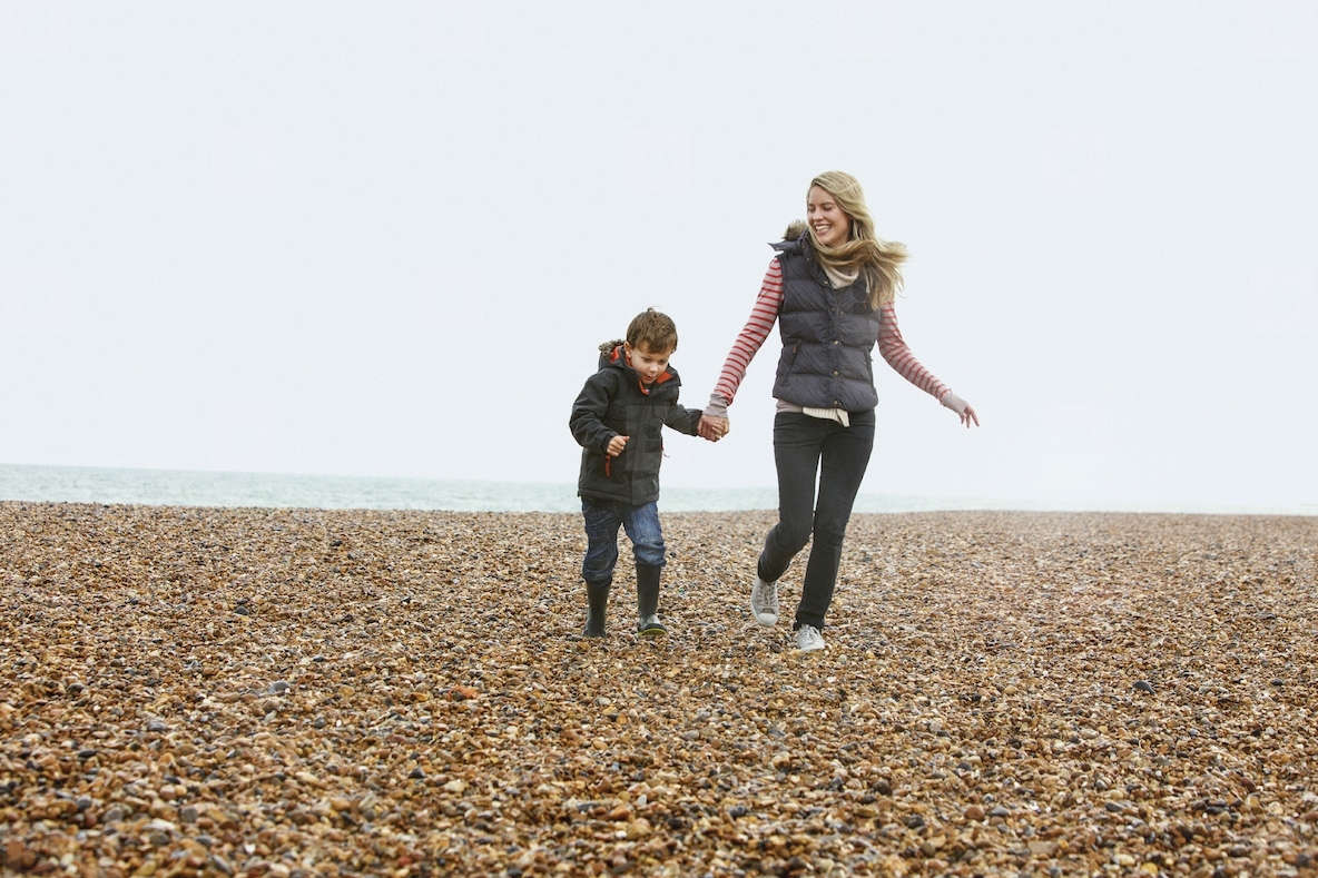 Carefree mother and son holding hands and walking on rocky winter beach
