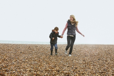 Carefree mother and son holding hands and walking on rocky winter beach