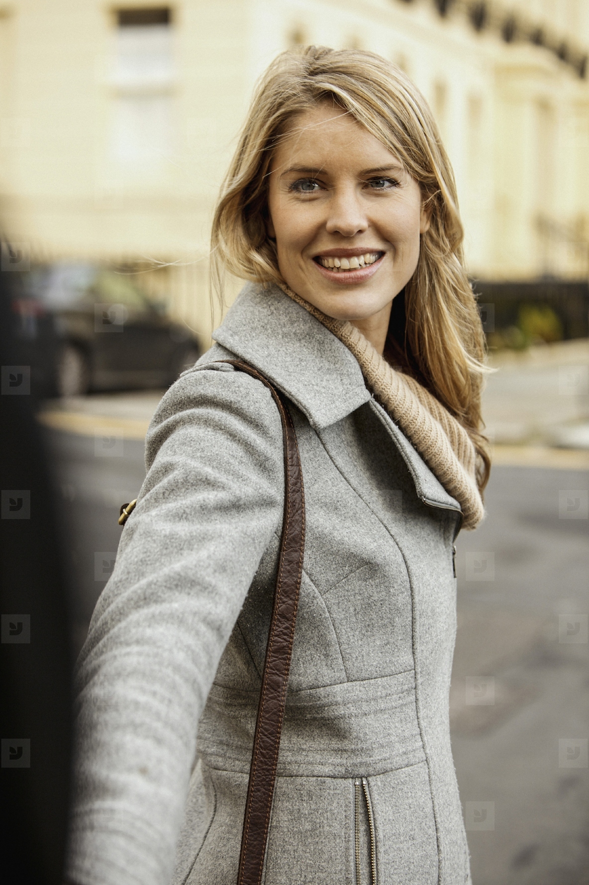 Beautiful blond woman in gray coat turning and smiling on sidewalk