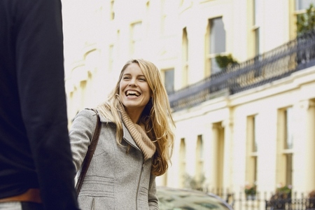 Carefree blond woman laughing in street and turning to man in foreground
