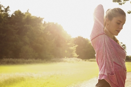 Beautiful woman stretching arm in sunny summer park