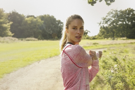 Portrait of beautiful blond woman stretching arm in sunny park